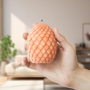 May include: A peach-colored dragon egg candle with a black wick. The candle is shaped like a dragon egg with a textured surface.