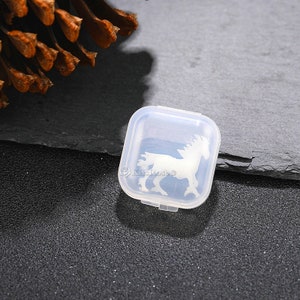 Op de afbeelding: Een vierkante, transparante plastic doos met een wit paard silhouet op de deksel. De doos is gesloten en staat op een donkergrijs oppervlak.