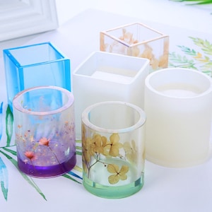 May include: Five clear resin moulds for making candles or other crafts. The moulds are in different shapes, including square and round. Some of the moulds have dried flowers inside.