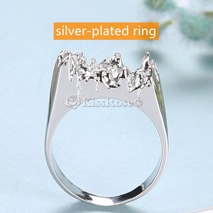 May include: Silver-plated ring with a textured, mountain-like design. The ring is a statement piece with a unique and modern style.