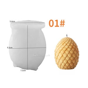 May include: A white silicone mold for making a candle shaped like a dragon egg. The mold is 7.3 cm wide, 6.3 cm tall, and 5.4 cm in diameter. The mold is shown next to a finished candle, which is a light brown color and has a textured surface.