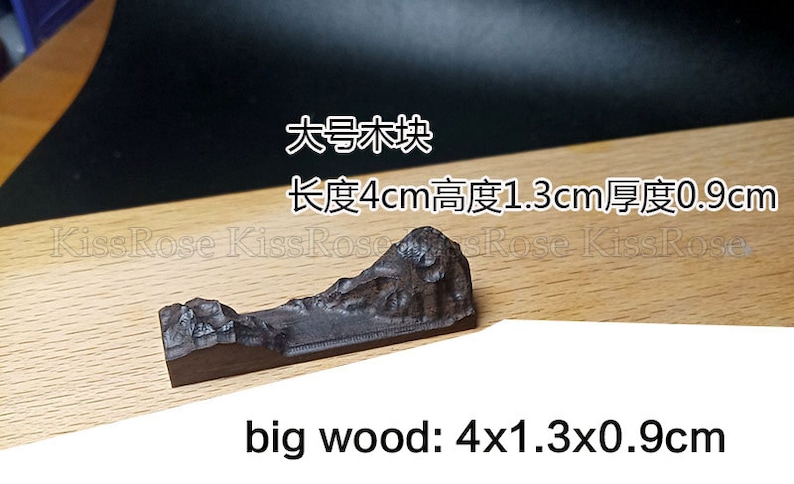 May include: A dark brown wooden mountain sculpture. The sculpture is 4 inches long, 1.3 inches high, and 0.9 inches thick. The text "big wood: 4x1.3x0.9cm" is written below the sculpture.