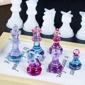 K&ouml;nnte beinhalten: Ein Set aus bunten gl&auml;sernen Schachfiguren, darunter K&ouml;nig, Dame, Springer, Turm und Bauer. Die Figuren sind durchscheinend und haben einen Farbverlauf, darunter Lila, Blau und Rosa.