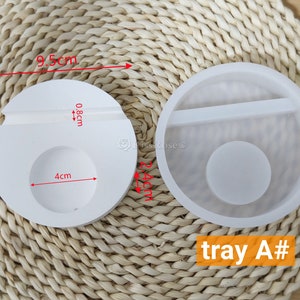 May include: Two white silicone molds for resin crafts. The mold on the left is 9.5 cm wide and has a 4 cm circle and a 0.8 cm slot. The mold on the right is a tray with a 4 cm circle and a divider. The text "tray A#" is visible in the image.