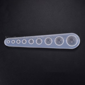 May include: A clear silicone mold with nine round cavities of varying sizes. The mold is designed for creating resin jewelry or other crafts.