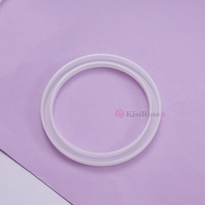 May include: A white silicone ring mold with a double ring design. The mold is on a purple surface.