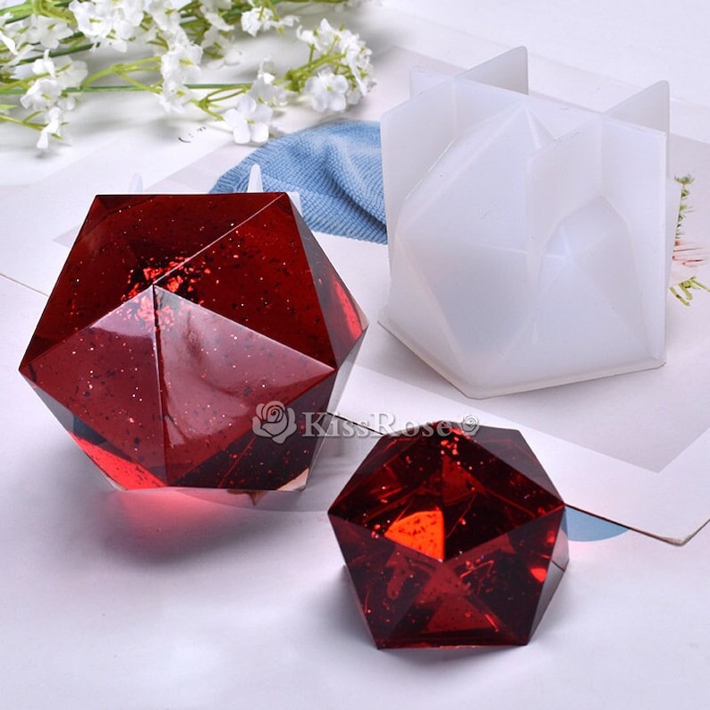 K&ouml;nnte beinhalten: Zwei rote geometrische Harzornamente und eine wei&szlig;e Silikonform zum Herstellen von geometrischen Harzornamenten.