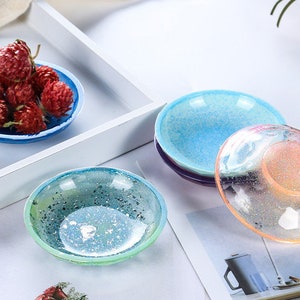 Op de afbeelding: Vier kleine, ronde, decoratieve schalen met een gespikkelde, iriserende afwerking. De schalen zijn in tinten blauw, groen en roze.