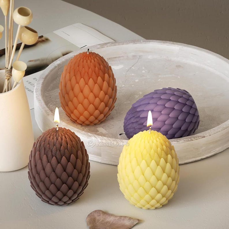May include: Three dragon egg-shaped candles in orange, purple, and yellow. The candles are lit and have a textured, scaly design.