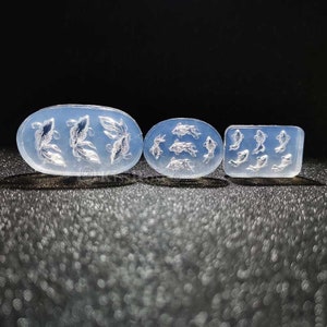 Könnte beinhalten: Drei transparente Silikonformen mit erhabenen Fischdesigns. Die Formen sind oval und rechteckig.