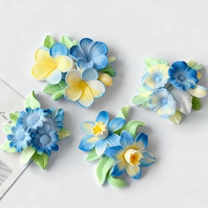 May include: Four floral arrangements featuring blue, yellow, and white flowers with green leaves. The flowers have a detailed, textured appearance. The arrangements are set against a white background, creating a clean and bright aesthetic.