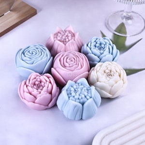 Puede incluir: Un conjunto de siete flores de jabón hechas a mano en varios tonos de rosa, azul y blanco. Las flores tienen forma de rosas, peonías y lirios.