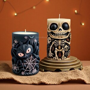 Puede incluir: Dos velas de pilar con temática de Halloween. Una es negra con un diseño de gato y telaraña. La otra es blanquecina con un diseño de esqueleto. Ambas velas tienen una mecha y están sobre una superficie marrón.