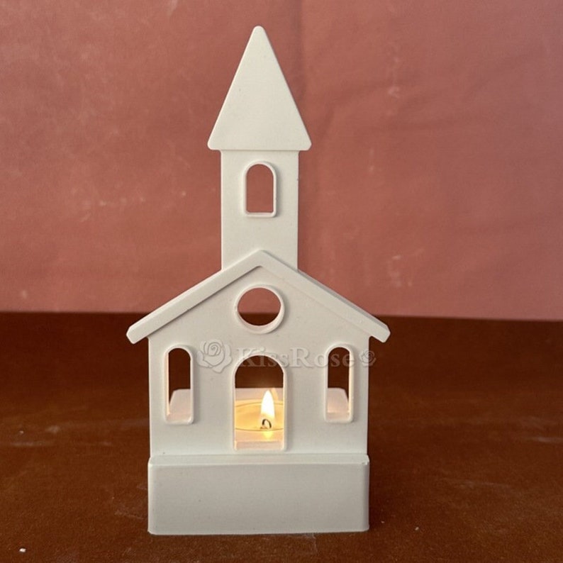 May include: White ceramic church-shaped candle holder with a tealight candle inside. The holder has a steeple and windows.