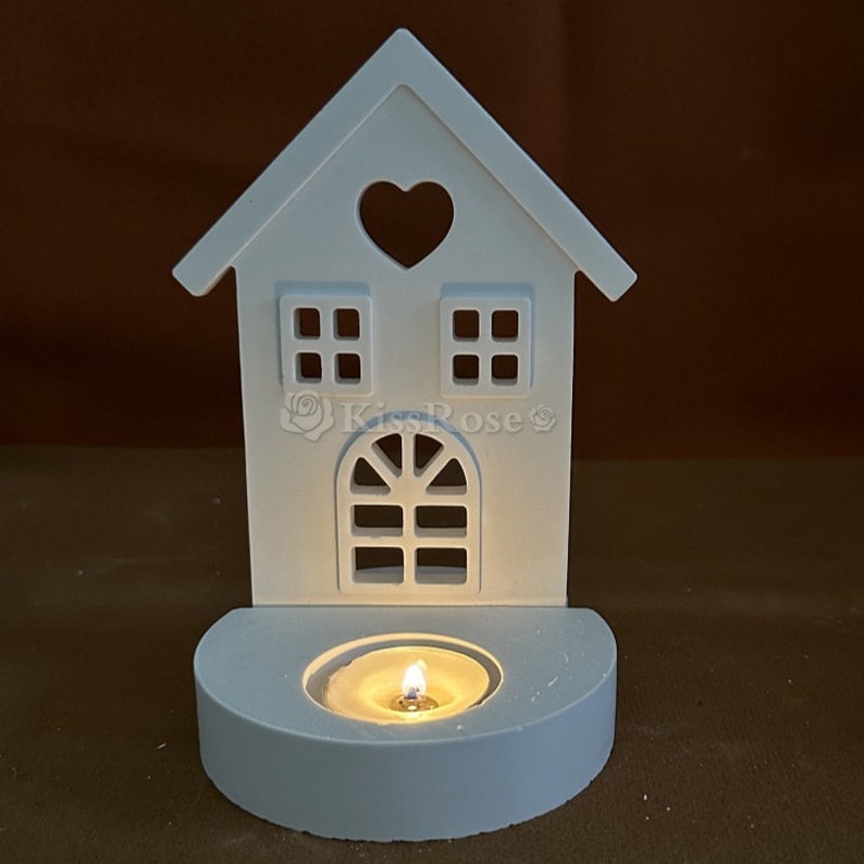 May include: White ceramic house shaped candle holder with a heart cutout and a small window. The holder has a tealight candle inside.