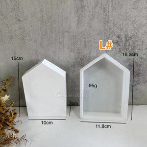 K&ouml;nnte beinhalten: Zwei wei&szlig;e hausf&ouml;rmige Silikonformen zum Basteln. Die gr&ouml;&szlig;ere Form ist 16,2 cm hoch, 11,8 cm breit und 3 cm tief. Die kleinere Form ist 15 cm hoch, 10 cm breit und 3 cm tief. Die Formen sind mit "L#" und "95g" gekennzeichnet.