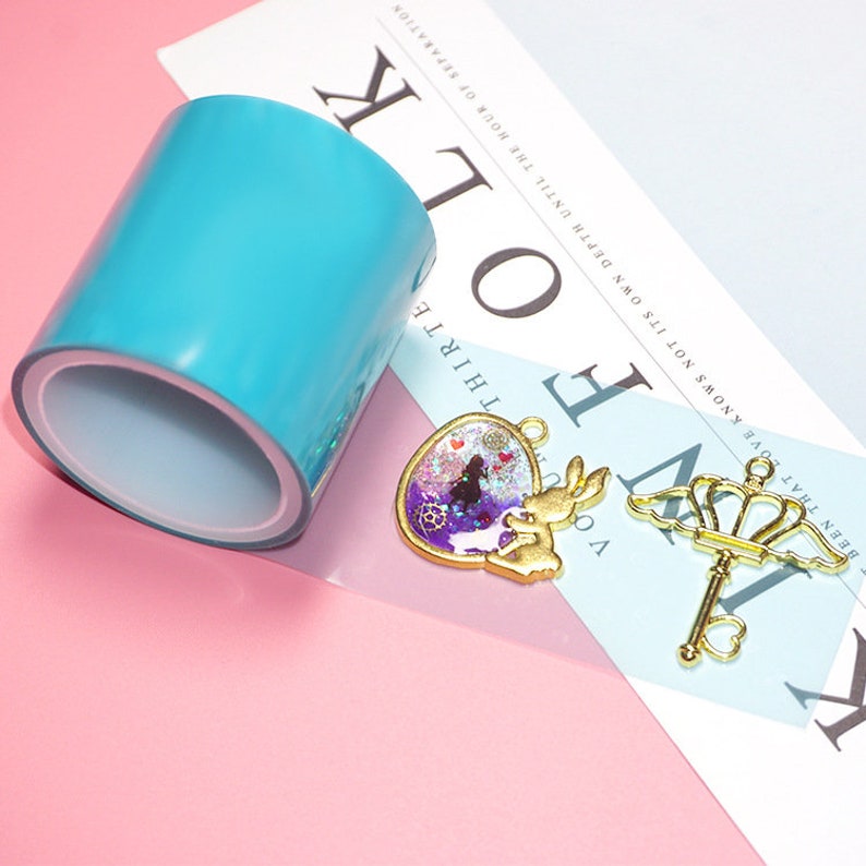 Pode incluir: Um rolo de fita de resina azul transparente, um pingente dourado com um design de resina roxo e azul, e uma chave dourada com uma coroa no topo.