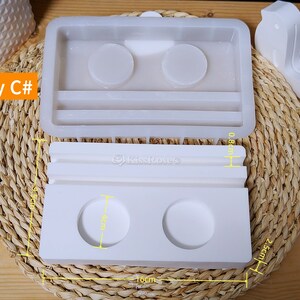May include: White silicone mold for making a tray with two round compartments and a rectangular section. The mold measures 10 cm wide, 2.5 cm high, and 8 cm long. The tray is labeled "tray C#"