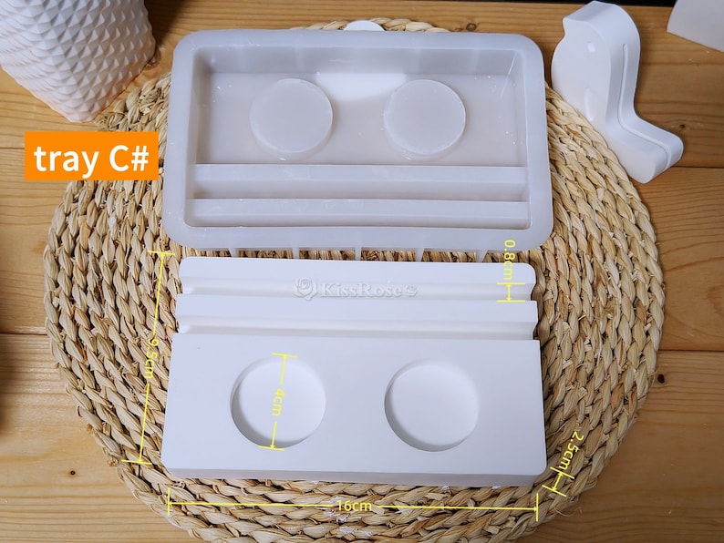 May include: White silicone mold for making a tray with two round compartments and a rectangular section. The mold measures 10 cm wide, 2.5 cm high, and 8 cm long. The tray is labeled "tray C#"