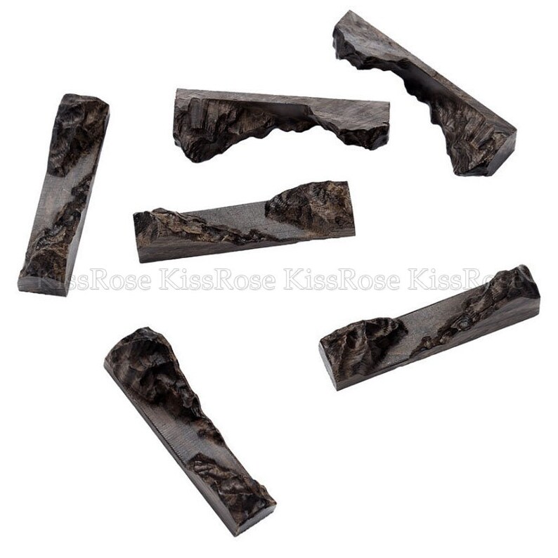 May include: Six dark brown wooden chopsticks with a mountain range design. The chopsticks are arranged in a scattered pattern on a white background.