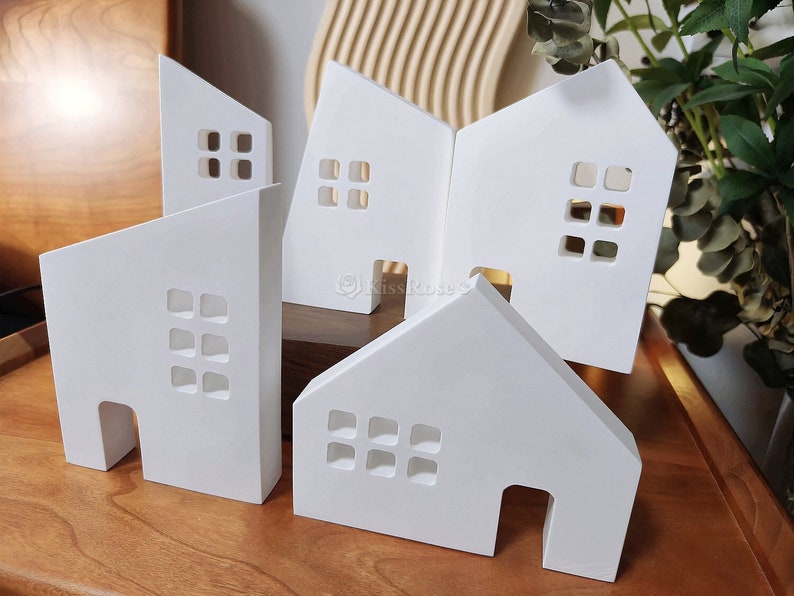 May include: Five white wooden houses with cut-out windows and doors. The houses are arranged in a staggered pattern on a wooden surface.