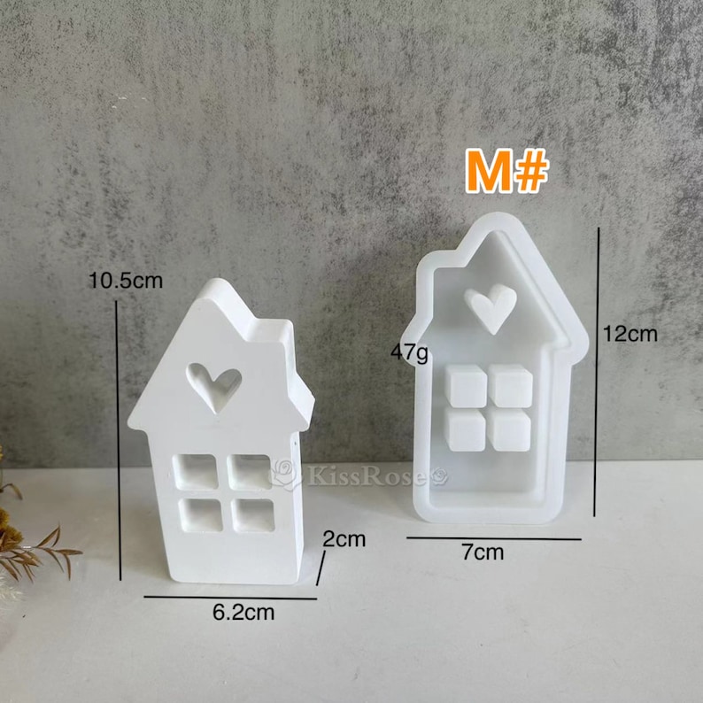 May include: Two white plastic molds shaped like houses with heart cutouts and window details. The larger mold is 12 cm tall and 7 cm wide. The smaller mold is 10.5 cm tall and 6.2 cm wide. Both molds are labeled "M#"