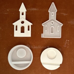 May include: Two white silicone molds for resin crafts. One mold is shaped like a church building with a pointed roof and windows. The other mold is a round shape with a smaller circle in the center and a rectangular shape below it.