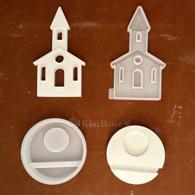 May include: Two white silicone molds for resin crafts. One mold is shaped like a church building with a pointed roof and windows. The other mold is a round shape with a smaller circle in the center and a rectangular shape below it.