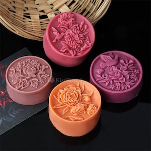 May include: Four decorative soap bars with floral and bird designs. The soaps are in shades of pink, red, and orange.