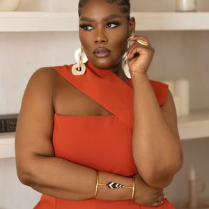 Model wearing Onika Orange Jumpsuit with asymmetrical neckline and African jewelry