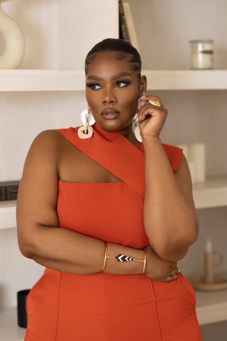 Model wearing Onika Orange Jumpsuit with asymmetrical neckline and African jewelry