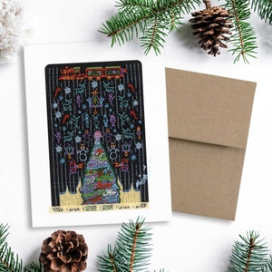 May include: A Christmas card with a black background featuring a colorful illustration of a Christmas tree, train, and various holiday-themed icons. The card is accompanied by a brown envelope and decorated with pine needles and a pine cone.