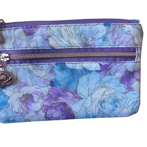 May include: A rectangular zipped pouch featuring a floral pattern in shades of light blue, periwinkle, and deep purple. The pouch includes a top zip closure and a front exterior zipped pocket with a metallic rose-shaped charm pull.