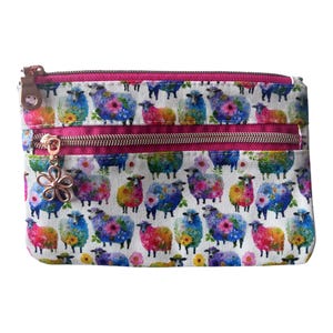 May include: A rectangular zipped pouch featuring a white fabric base with a repeating pattern of colourful sheep decorated with floral designs. The pouch includes a bright pink fabric trim, metallic zips, and a flower-shaped metal zip pull.