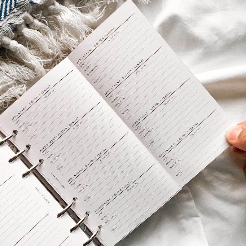 May include: A white planner with a black spiral binding. The planner has multiple pages with headings for "Appointment: Doctor/Dentist", "Date", "Reason", "Medication", "Notes", and "Follow Up".