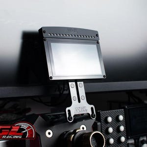 May include: A black racing simulator display screen mounted on a bracket. The screen is rectangular with a silver frame and is attached to a black base. The KGL Racing logo is visible.