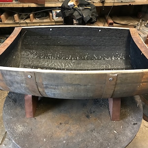 May include: A wooden barrel planter with a dark brown stain. The barrel is cut in half and has a white liner inside. The barrel is sitting on three wooden legs.