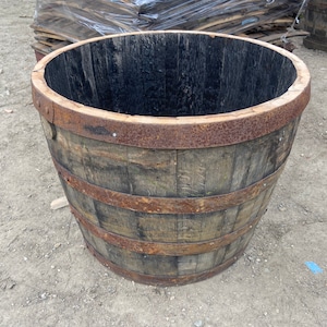 May include: A rustic wooden barrel planter with metal bands. The barrel is made of dark wood and has a natural finish. The metal bands are rusty and add a vintage look to the planter.