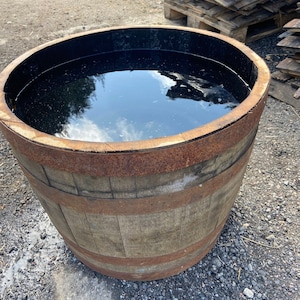 May include: A wooden barrel planter filled with water, reflecting the sky. The barrel has rusty metal bands and is weathered with age.