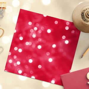 May include: A red background with white bokeh lights. The background is a flat surface with a gold cup, gold paper clips, pencils, and a gold bell on it.
