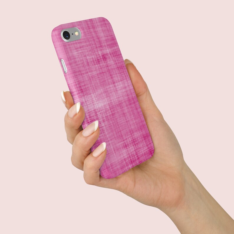 May include: A pink phone case with a textured linen design. The case is being held in a hand.