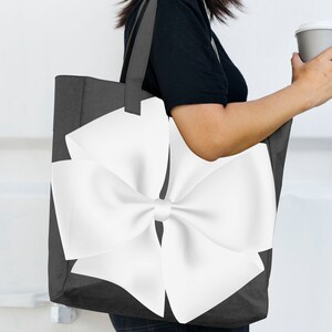 May include: A black tote bag with a large white bow on the front. The bag has a white handle.