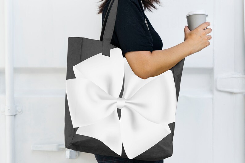 May include: A black tote bag with a large white bow on the front. The bag has a white handle.