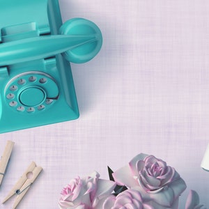 May include: A flat lay of a teal rotary phone, wooden clothespins, silver push pins, a white digital camera, and a bouquet of pink roses on a light purple textured background.