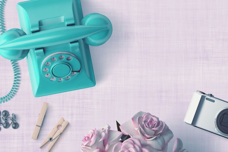 May include: A flat lay of a teal rotary phone, wooden clothespins, silver push pins, a white digital camera, and a bouquet of pink roses on a light purple textured background.
