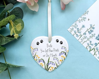 May include: White ceramic heart-shaped ornament with a floral design and the text "Belle You left Paw Prints on Our Hearts".