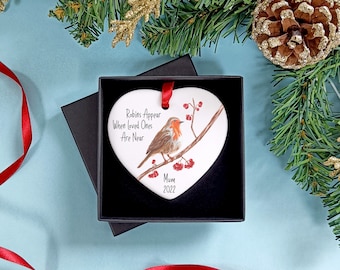 May include: A white heart-shaped ceramic ornament with a robin perched on a branch with red berries. The ornament has the text "Robins Appear When Loved Ones Are Near" and "Mum 2022".