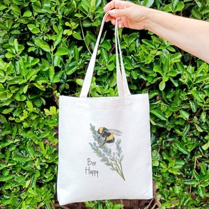 May include: A white tote bag with a bee and lavender design. The bag has the text "Bee Happy" printed on it.