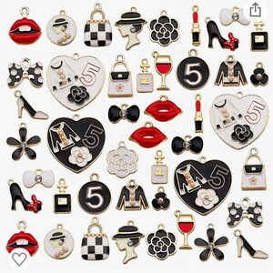 May include: A collection of 36 black and white enamel charms with gold accents. The charms feature various designs, including lips, bows, flowers, handbags, wine glasses, and the number 5.