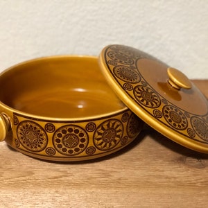 May include: A brown ceramic casserole dish with a lid. The dish has a geometric pattern in brown and black. The lid has a knob on top.